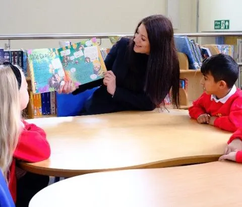 A teacher reads a story book to two primary school children.