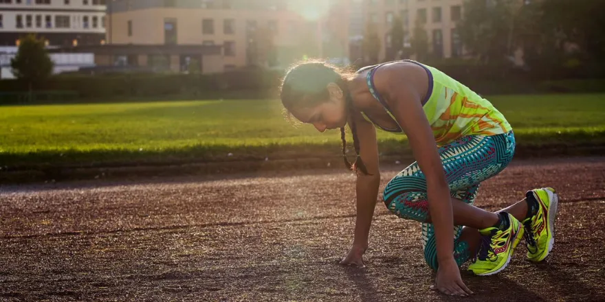 Girl in activewear crouches on running track.