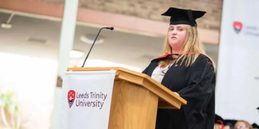 Blonde female student delivers speech in graduation cap and gown.