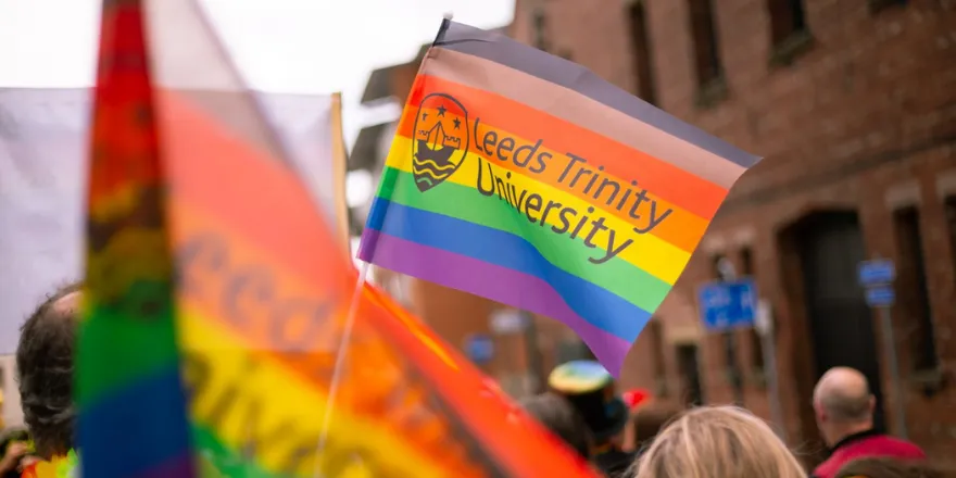 Rainbow flag with Leeds Trinity University logo is held in the air.
