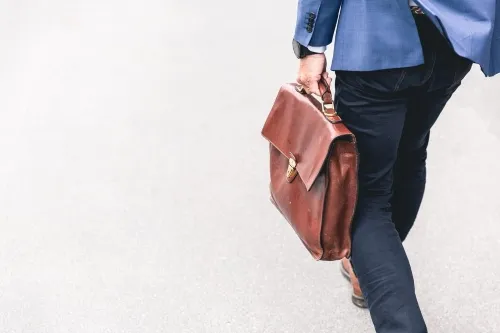 Person walking with brown leather bag .