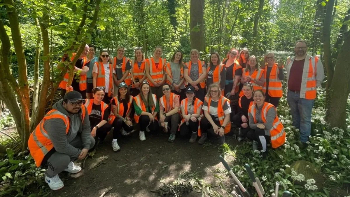 A large group of people wearing orange safety vests pose for a picture surrounded by trees.