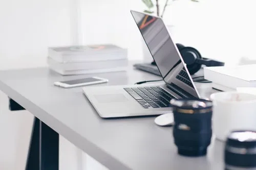 Desk with mug, laptop, mobile and books .