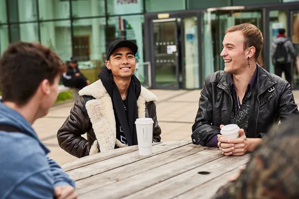 Students drinking coffee outside Main Campus entrance.