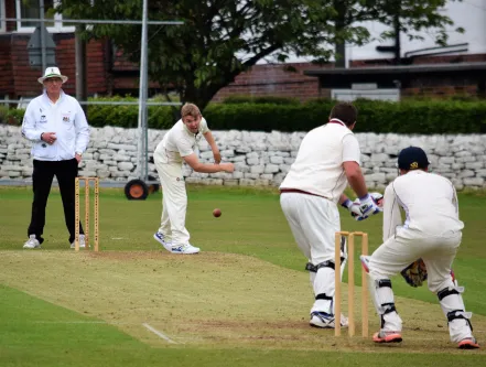 A group of people in white uniforms playing cricket on a green pitch.