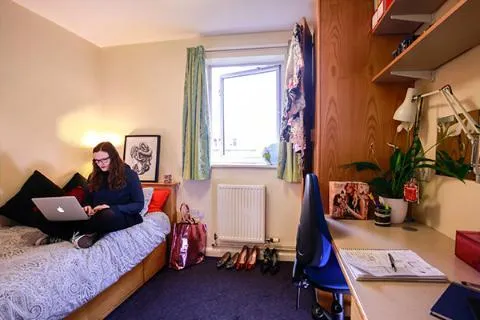 A student sat on her bed in a bedroom in Kirkstall Hall.