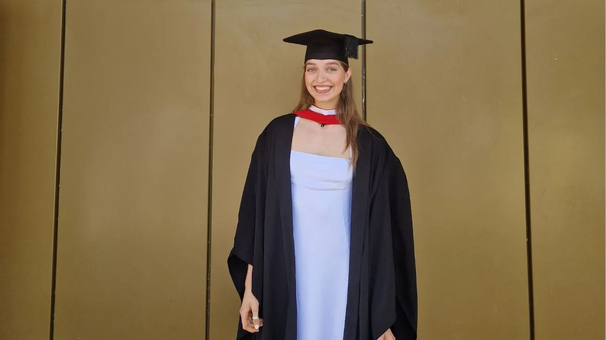 A girl wearing a black cap and gown over a white dress smile for a picture.