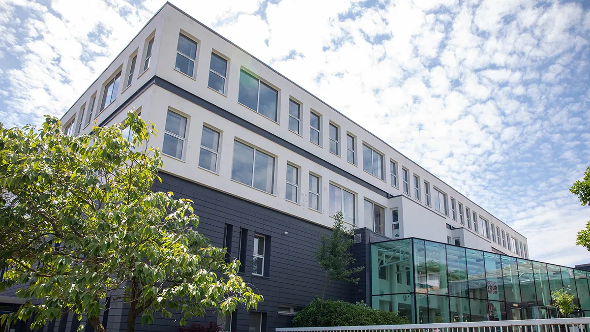 The Leeds Trinity University Main Reception building at the Main Campus in Horsforth, seen from a low angle. It is a grey and white building with a glass front entrance..