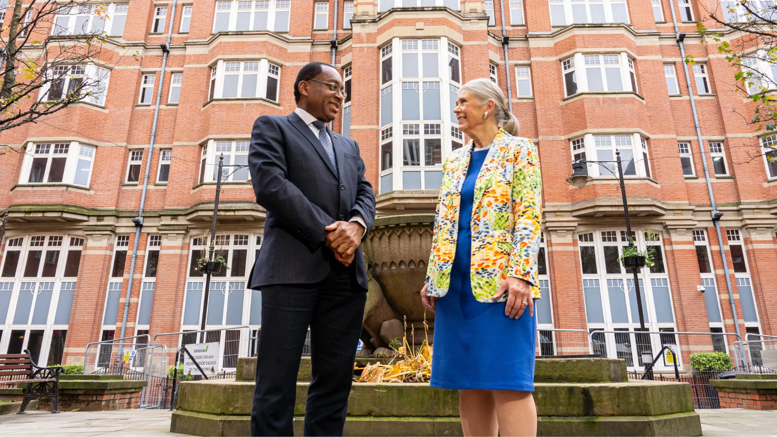 Man and woman, Professor Charles Egbu and Sandi Rhys Jones OBE outside the Leeds Trinity University city centre campus building.