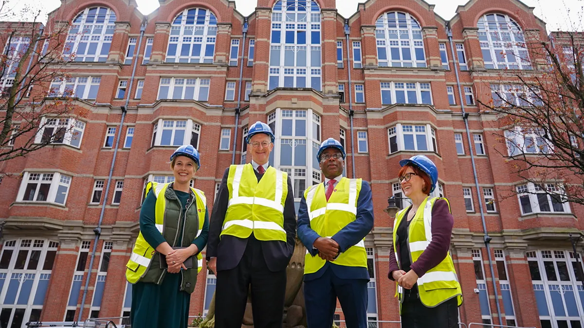A group of four people, two women and two men, posing in front of Leeds Trinity University city campus, wearing hard hats and high-vis vests..