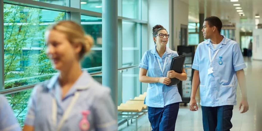 A female and male nurse walking in a corridor, with another female nurse in the foreground..