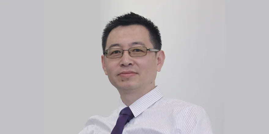 A headshot of a man with brown hair and glasses, sitting in front of a plain white wall.