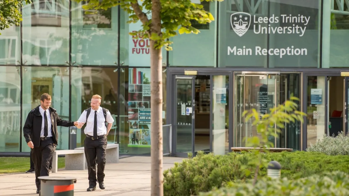 Two trainee prison officers in uniform walking outside University entrance.