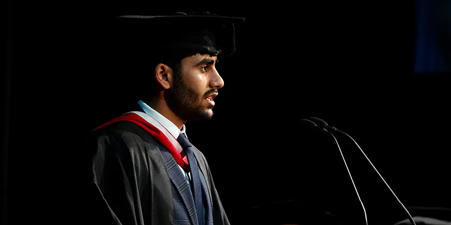 A student in graduation cap and gown giving the vote of thanks speech at Leeds Trinity University..