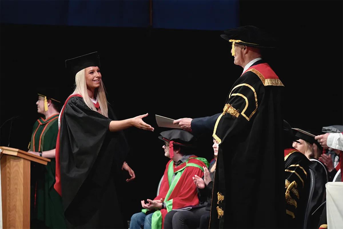 Student shaking hands with executive during graduation ceremony..