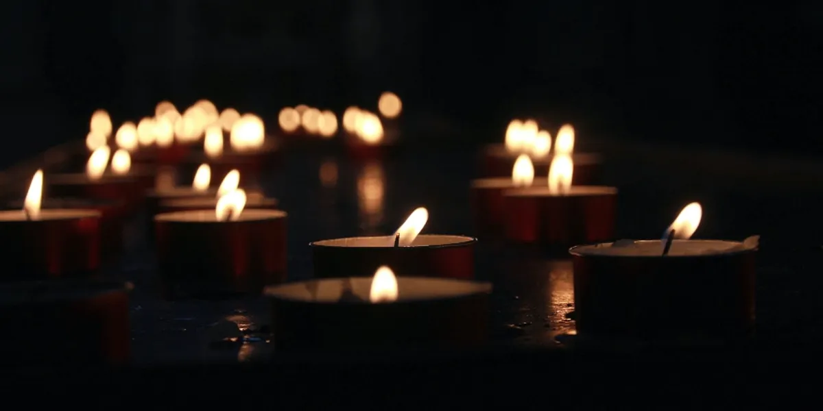 A number of lit tea light candles in a dark space.