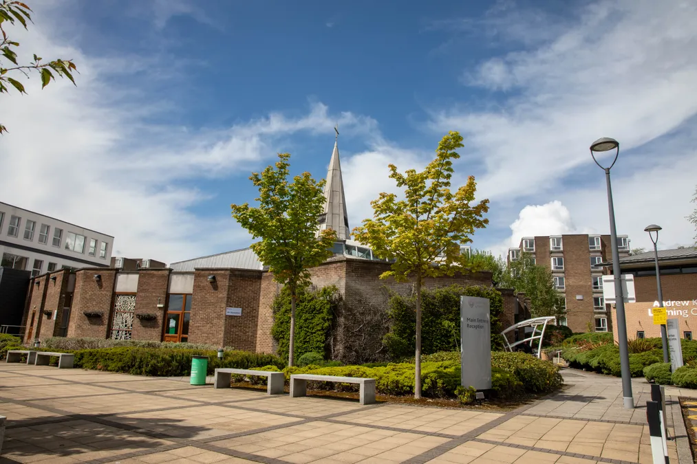 Exterior shot of Leeds Trinity University Chapel on its campus in Horsforth, with green trees and signage in the forefront.